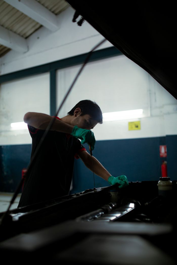 about-img Mechanic checks engine oil in a car inside an auto garage, highlighting routine maintenance.