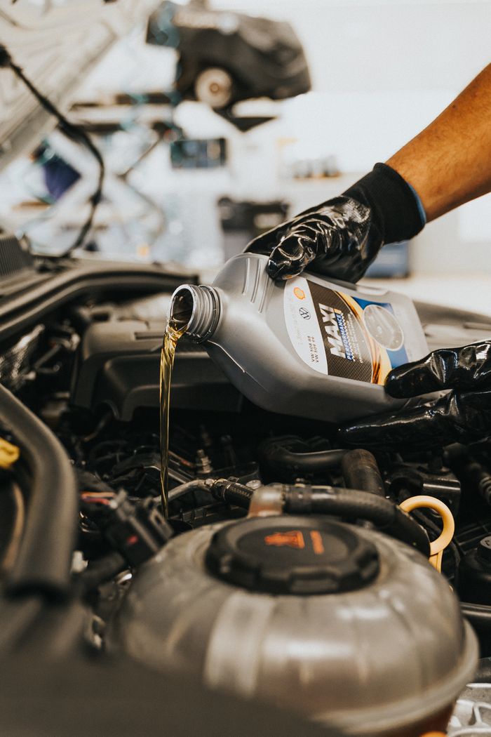 creative-approach-img A close-up of a mechanic in gloves pouring engine oil into a car engine, showcasing automotive maintenance.